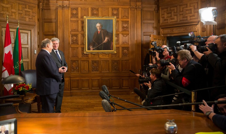 His Highness the Aga Khan and the Right Honourable Stephen Harper, the Prime Minister of Canada, face eager cameras at the Canadian Parliament Building on Thursday, 27 February, 2014. An oil on canvas painting of The Right Honourable Sir John Alexander Macdonald, Prime Minister (1867-1873; 1878-1891) adorns a wall as part of the House of Commons Heritage Collection, while the Ismaili Imamat and Canadian Flags form a backdrop in this historical photo. Photo credit: The Office of the Prime Minister of Canada.