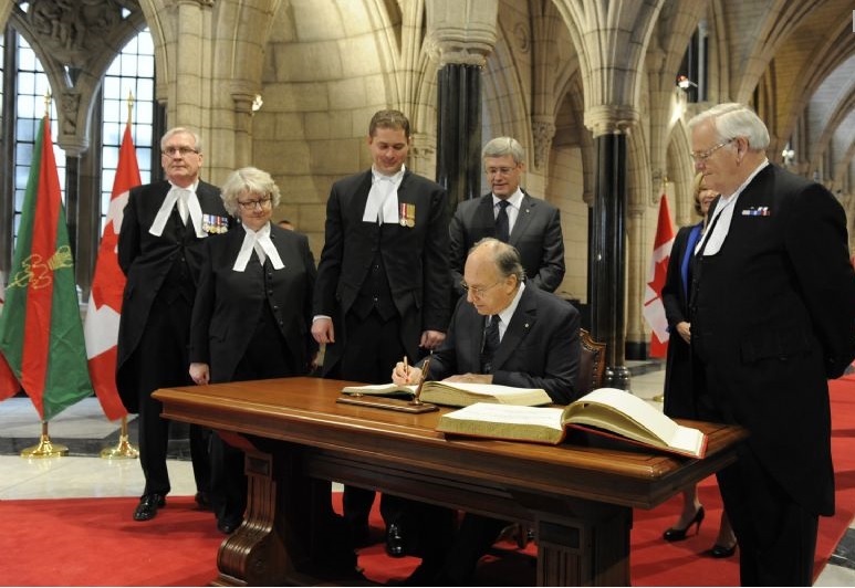 His Highness the Aga Khan signs the visitors books for the House of Commons and the Senate in the Canadian Parliament Rotunda as Prime Minister Stephen Harper, his wife Laureen Harper, The Honourable Andrew Scheer, Speaker of the House of Commons and the Honourable Noël Kinsella, Speaker of the Senate, and other individuals look on. Photo credit: TheIsmaili/Gary Otte.